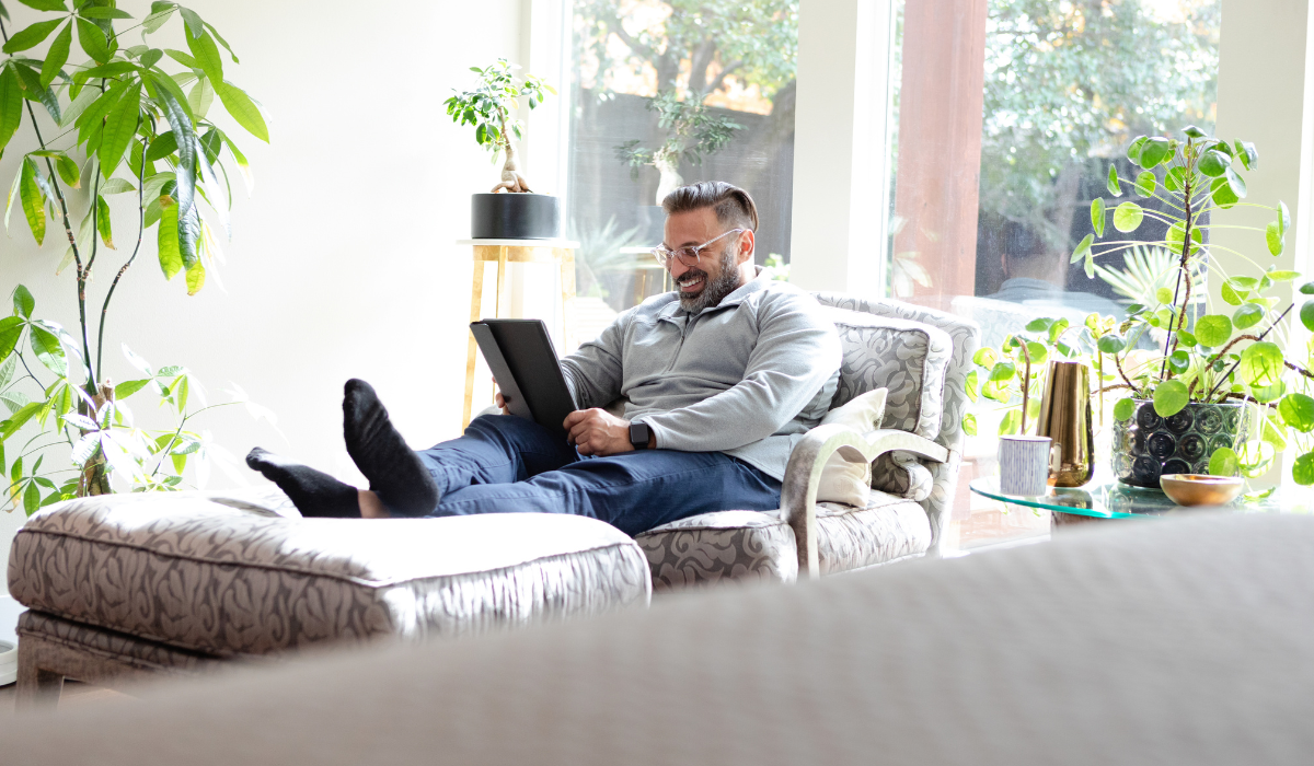 man with glasses on the couch looking at this tablet smiling